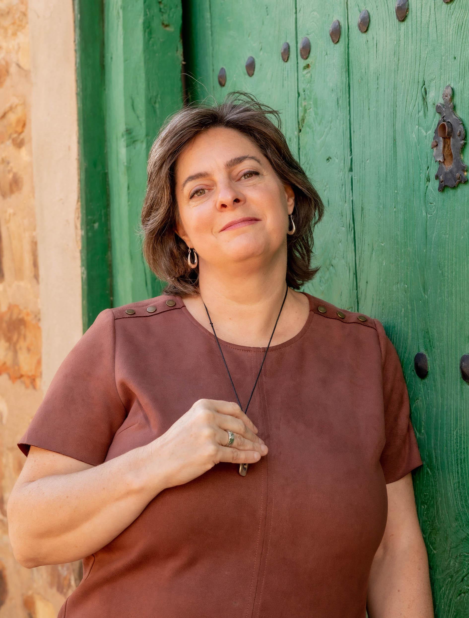 (2172) Christi Byerly, founder of Awaken is looking at the camera, holding a pendant necklace and smiling.